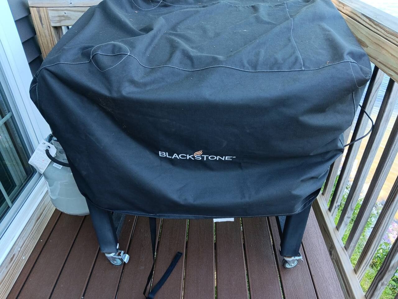 A barbecue grill with a BLACKSTONE brand cover on a wooden deck.