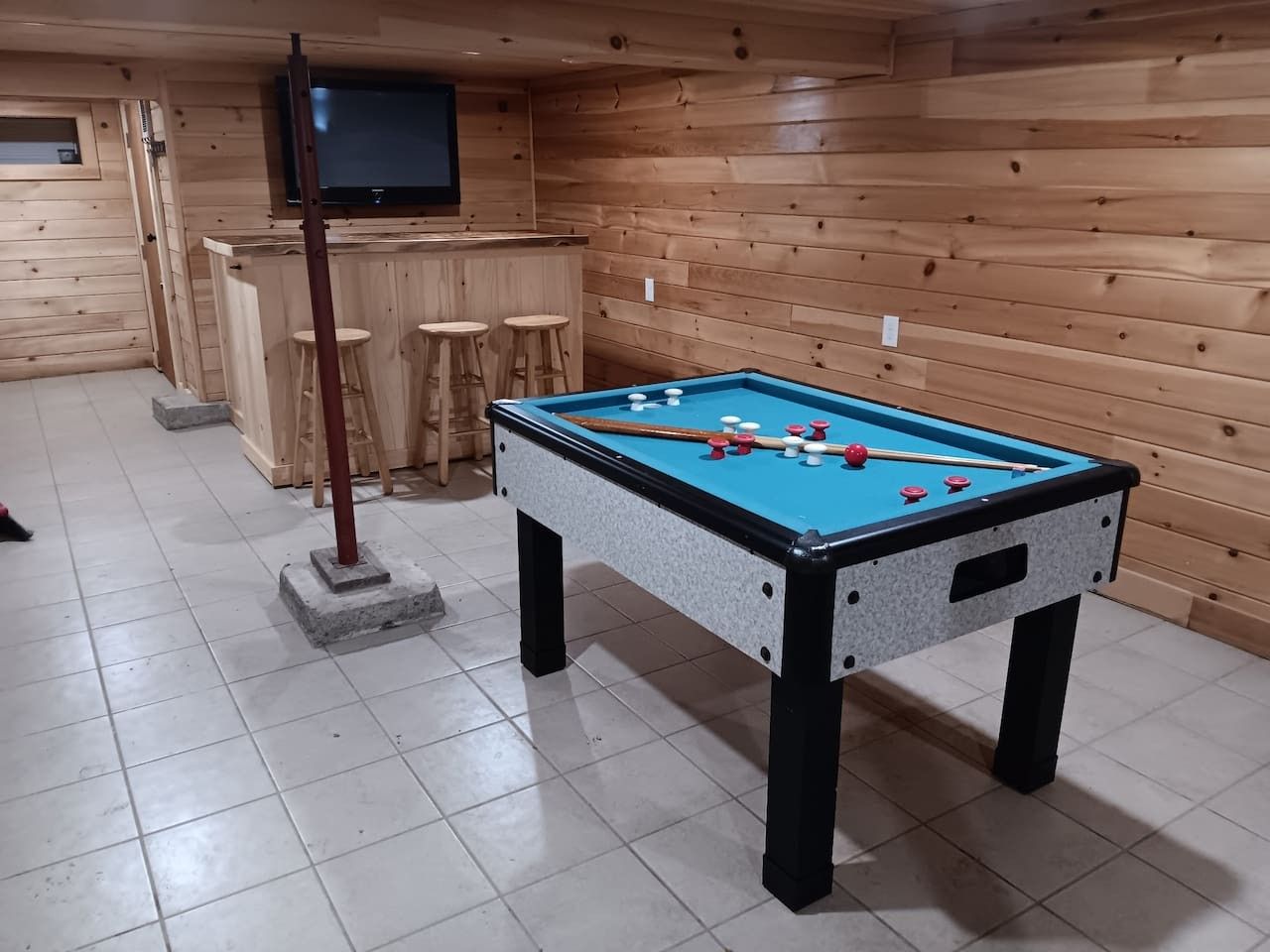 Taula de bitlles amb feltre blau, envoltada de parets de fusta i un terra de rajola.
