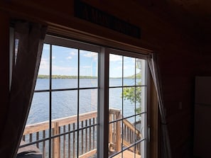 A room with a large window overlooking a body of water, a wooden deck outside, and a sign above the window.