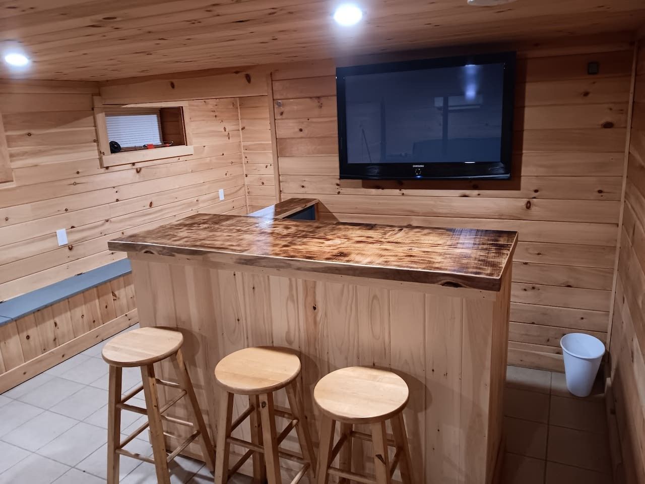 A wooden interior with a bar area featuring stools and a television mounted on the wall.