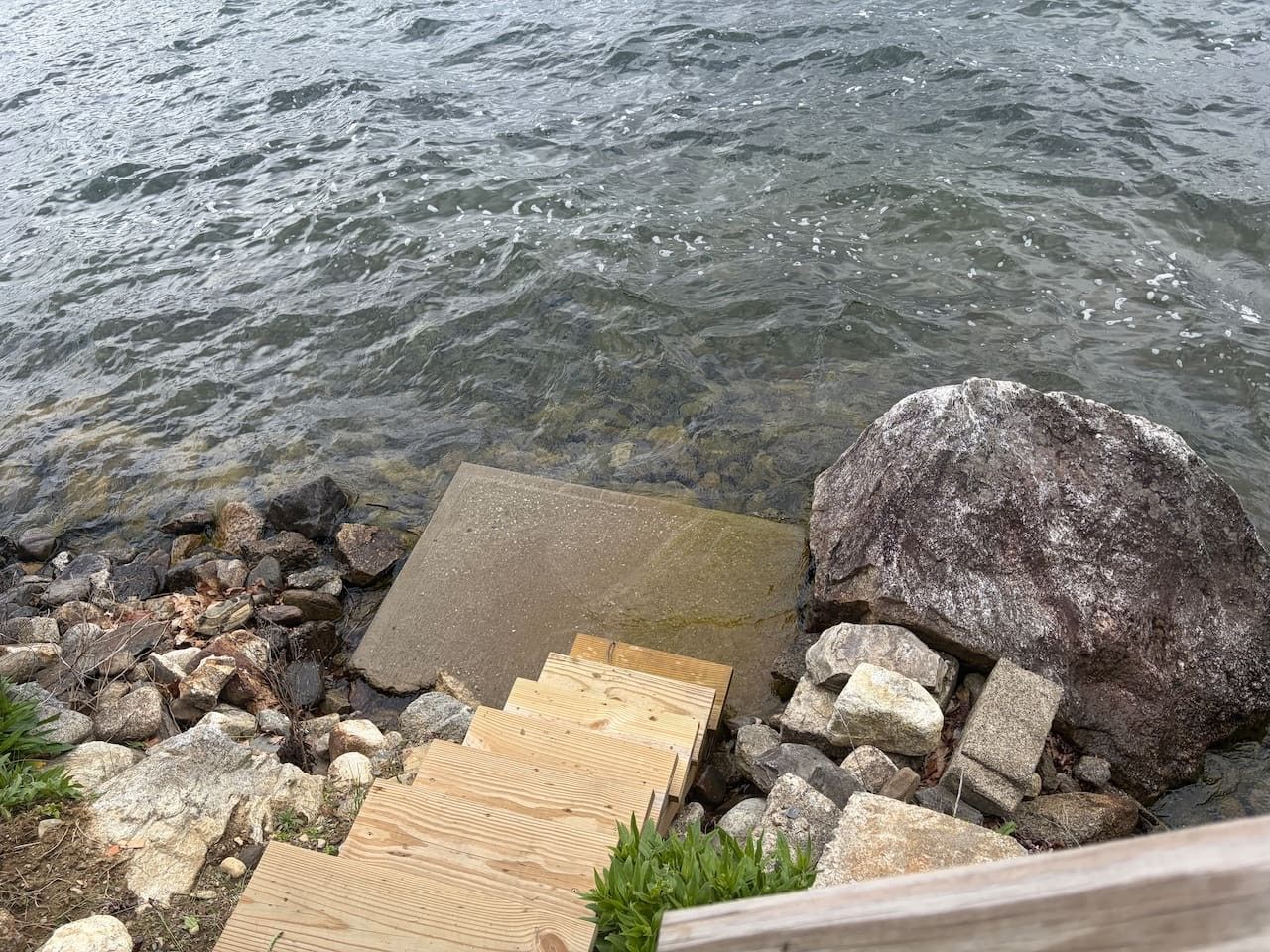 A wooden dock extending into a body of water, surrounded by rocks and a large boulder.