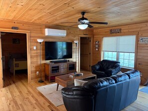 Interior de uma cabana de madeira com televisão, sofá e ventilador de teto.