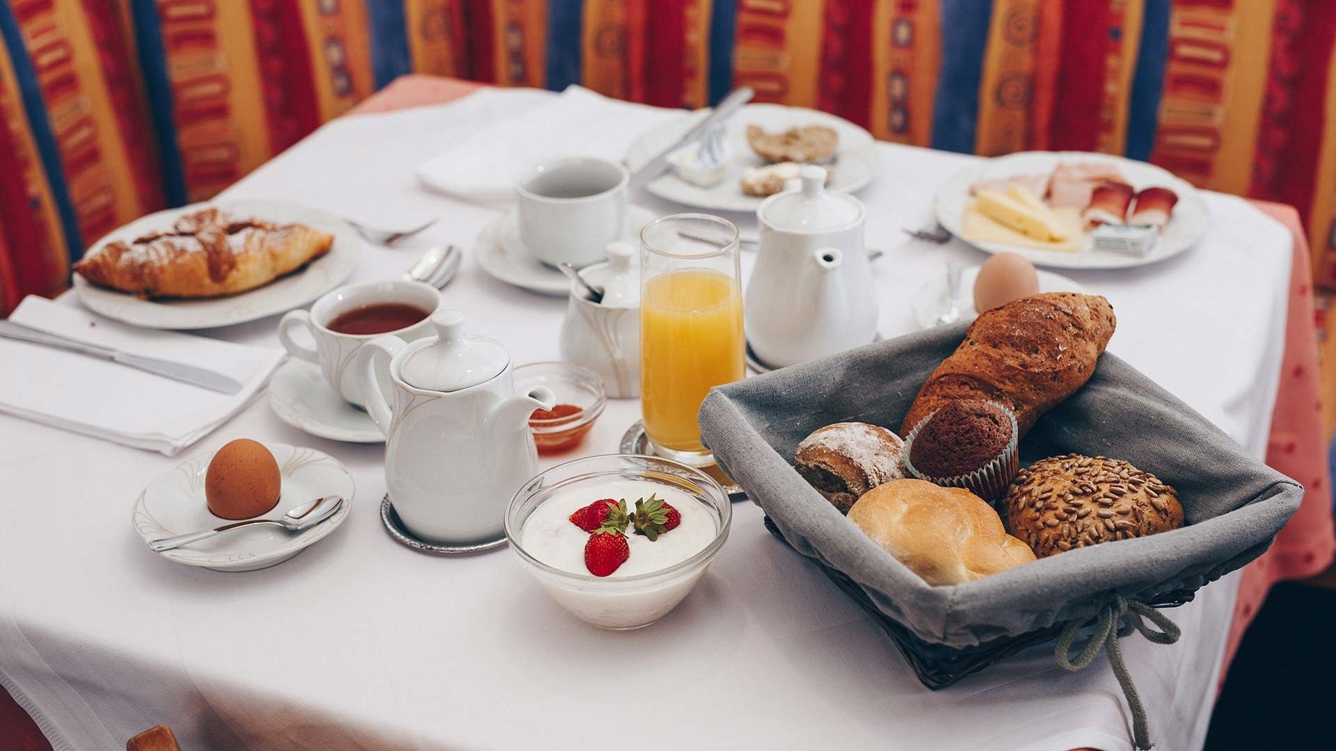 Une table de petit-déjeuner avec divers aliments, notamment des viennoiseries, du pain et un panier de fruits.