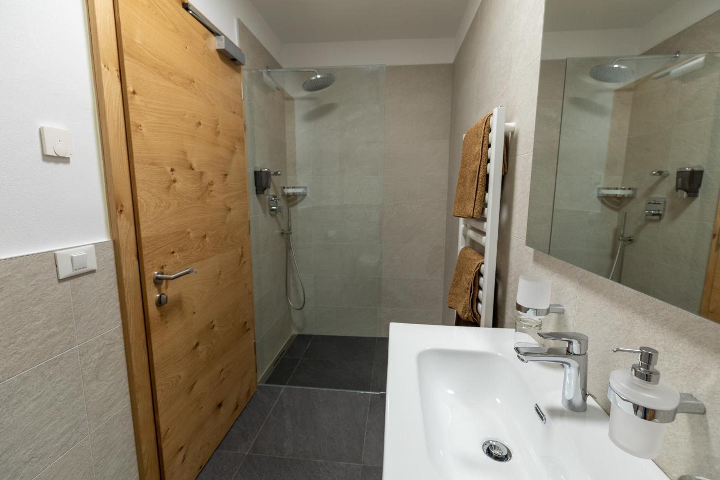 A bathroom with a wooden door, a shower, a sink with a mirror, and towels.