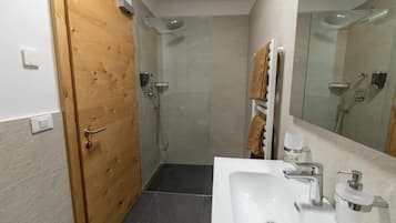 A bathroom with a wooden door, a shower, a sink with a mirror, and towels.