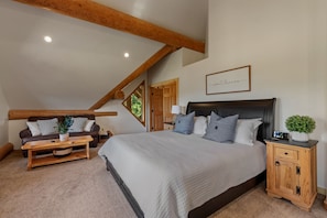 A bedroom with a large bed, a wooden headboard, a nightstand, a bedside table, and a window with a view of greenery. - Bottle Bay Beauty | Lake Views Near Sandpoint (Sagle)