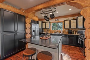 A modern kitchen with a central island, dark cabinetry, and a stone backsplash. - Bottle Bay Beauty | Lake Views Near Sandpoint (Sagle)