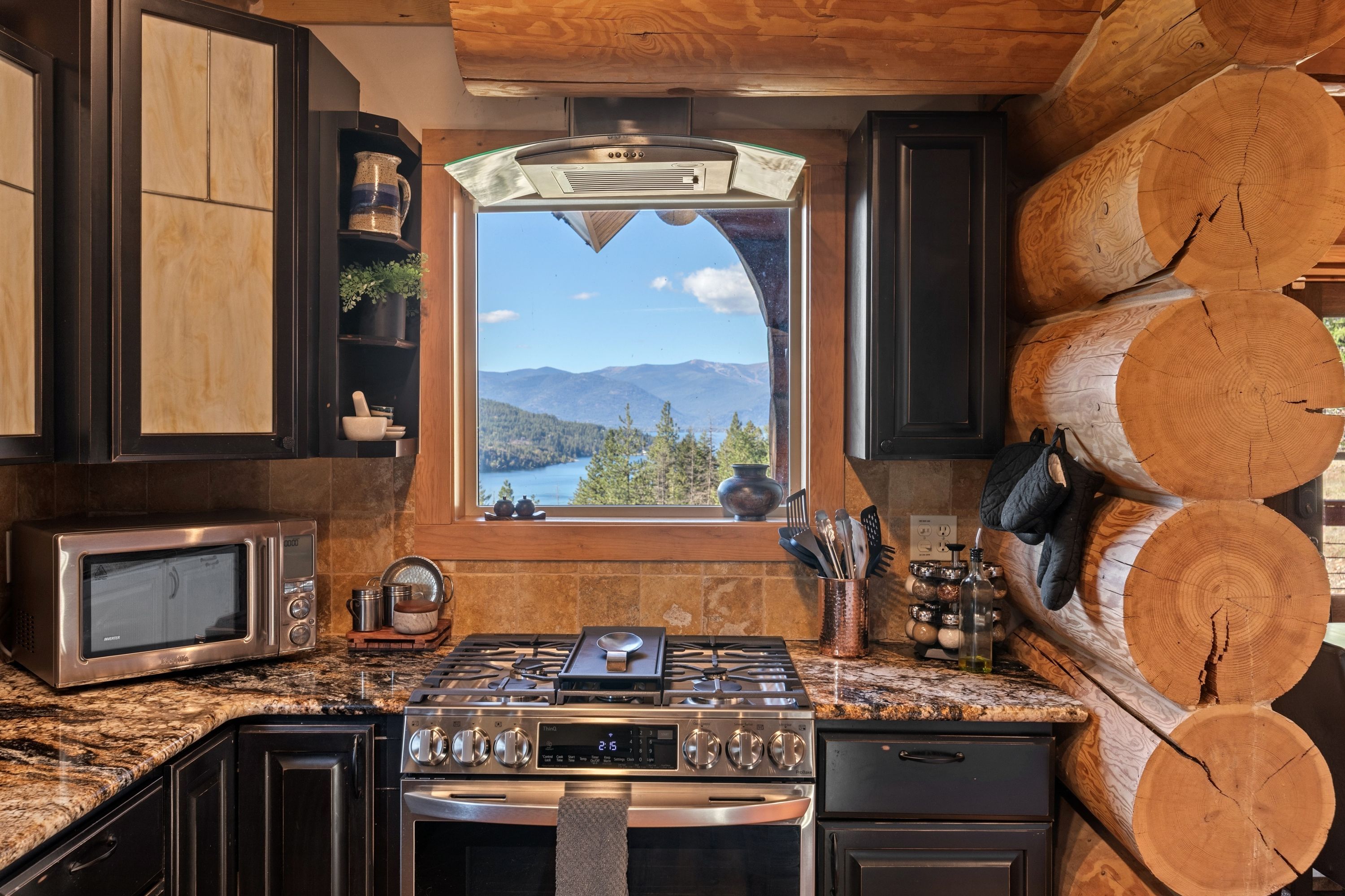 A kitchen with a stove, oven, microwave, and a window overlooking a mountainous landscape.