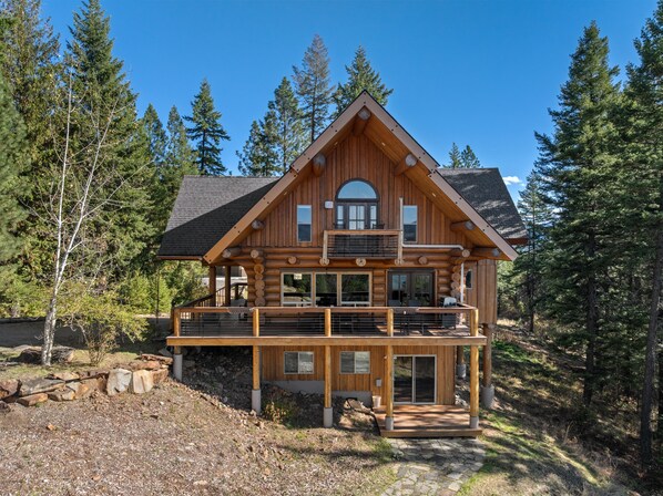 Een houten chalet met een balkon, grote ramen en een stenen fundering.