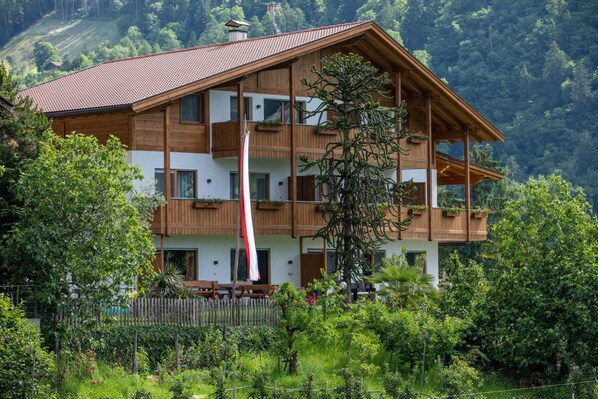 Ein mehrstöckiges Holzgebäude mit Balkonen, umgeben von üppiger Vegetation und einer Bergkulisse.