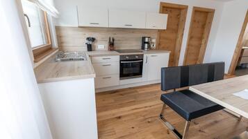 A modern kitchen with white cabinets, a stainless steel sink, a coffee maker, and a dining area with a bench and table.