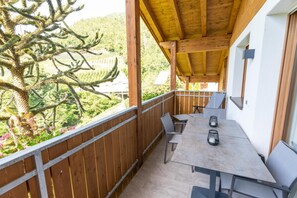 Ein Balkon mit Tisch und Stühlen mit Blick auf einen Garten mit einem großen Baum.