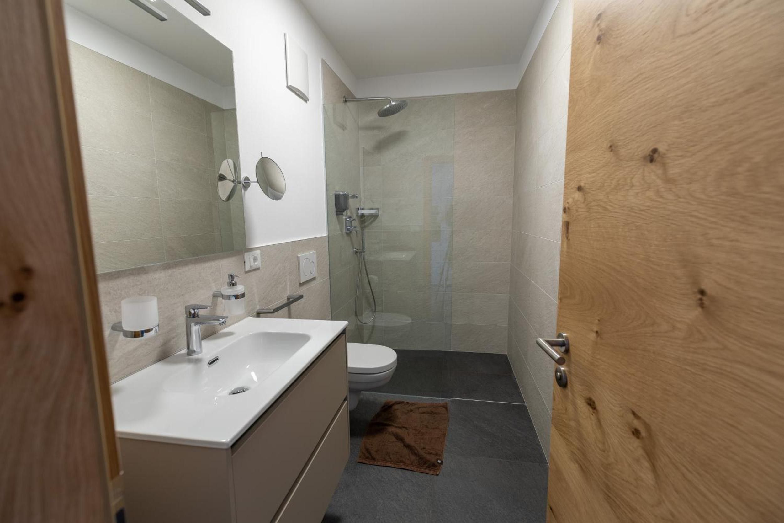 A modern bathroom with a white sink, mirror, and toilet, and a shower area with glass doors.