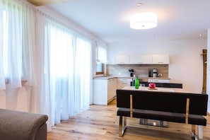 Ein modernes Wohnzimmer mit einer schwarzen Couch, einem Esstisch mit einem roten Apfel und einer Küche im Hintergrund.