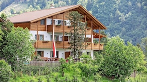 Ein mehrstöckiges Holzgebäude mit Balkonen, umgeben von üppiger Vegetation und einer Bergkulisse.