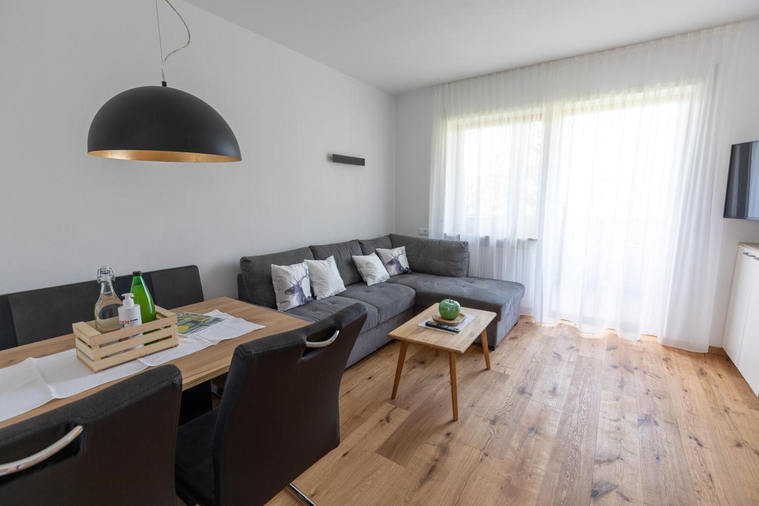 A modern living room with a grey sofa, a wooden coffee table, and a dining area with a wooden table and chairs.