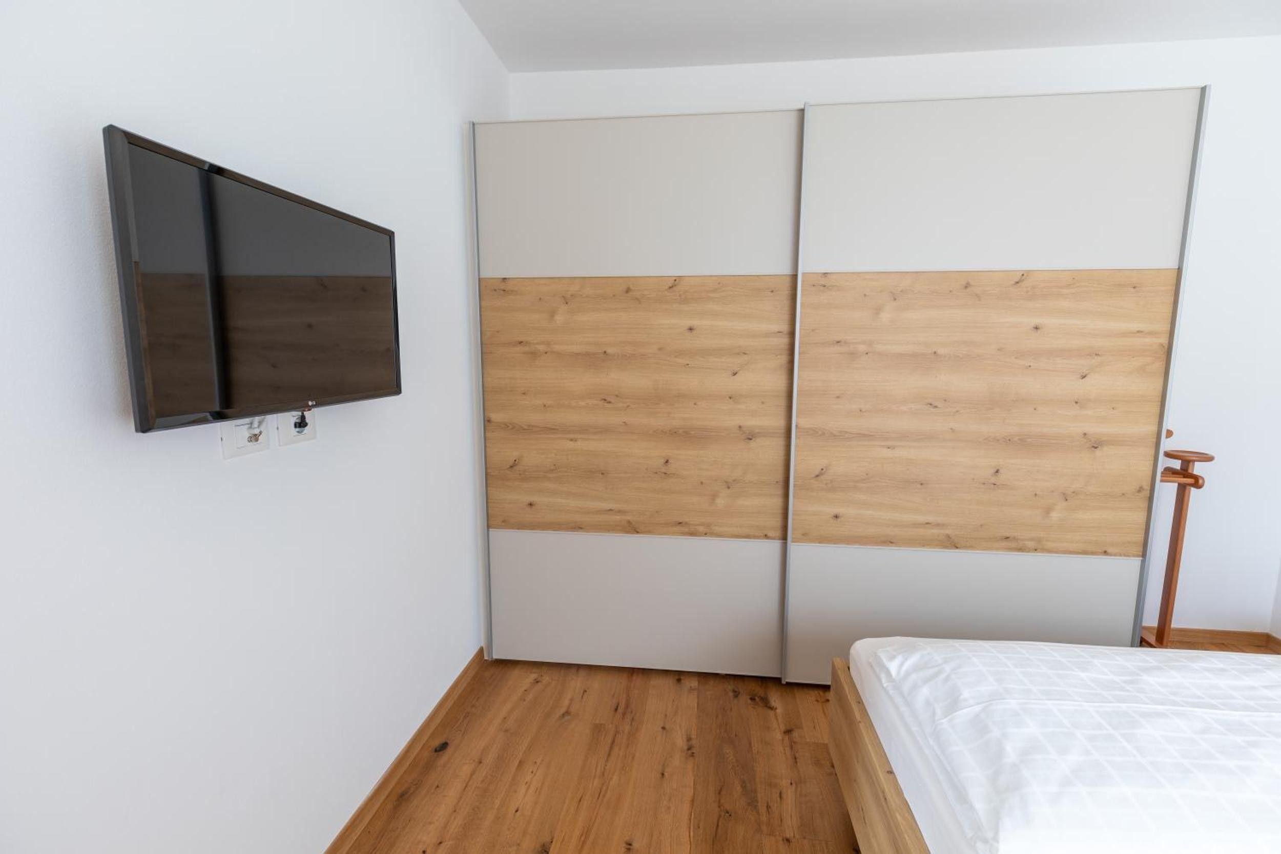 A bedroom with a bed, a TV mounted on the wall, and a wardrobe with a wooden panel design.