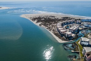 Luftaufnahme einer Küstenregion mit Sandstrand, einer Marina und einer Ansammlung von Gebäuden mit Balkonen.