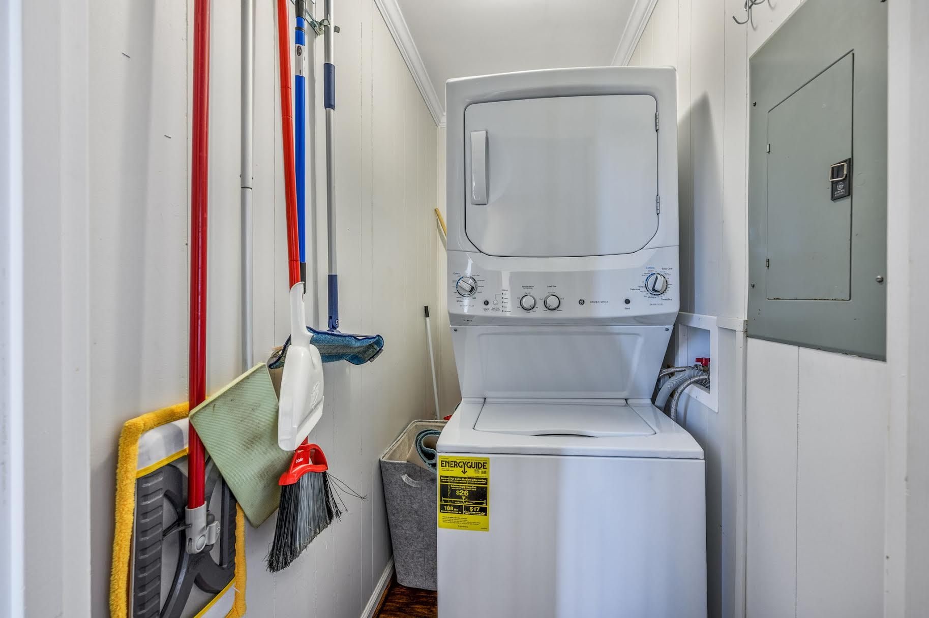 A laundry room with a front-loading washing machine, a mop, and a broom.