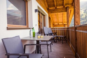 Ein überdachter Außenbereich mit Tisch und Stühlen, einer Flasche und Gläsern.