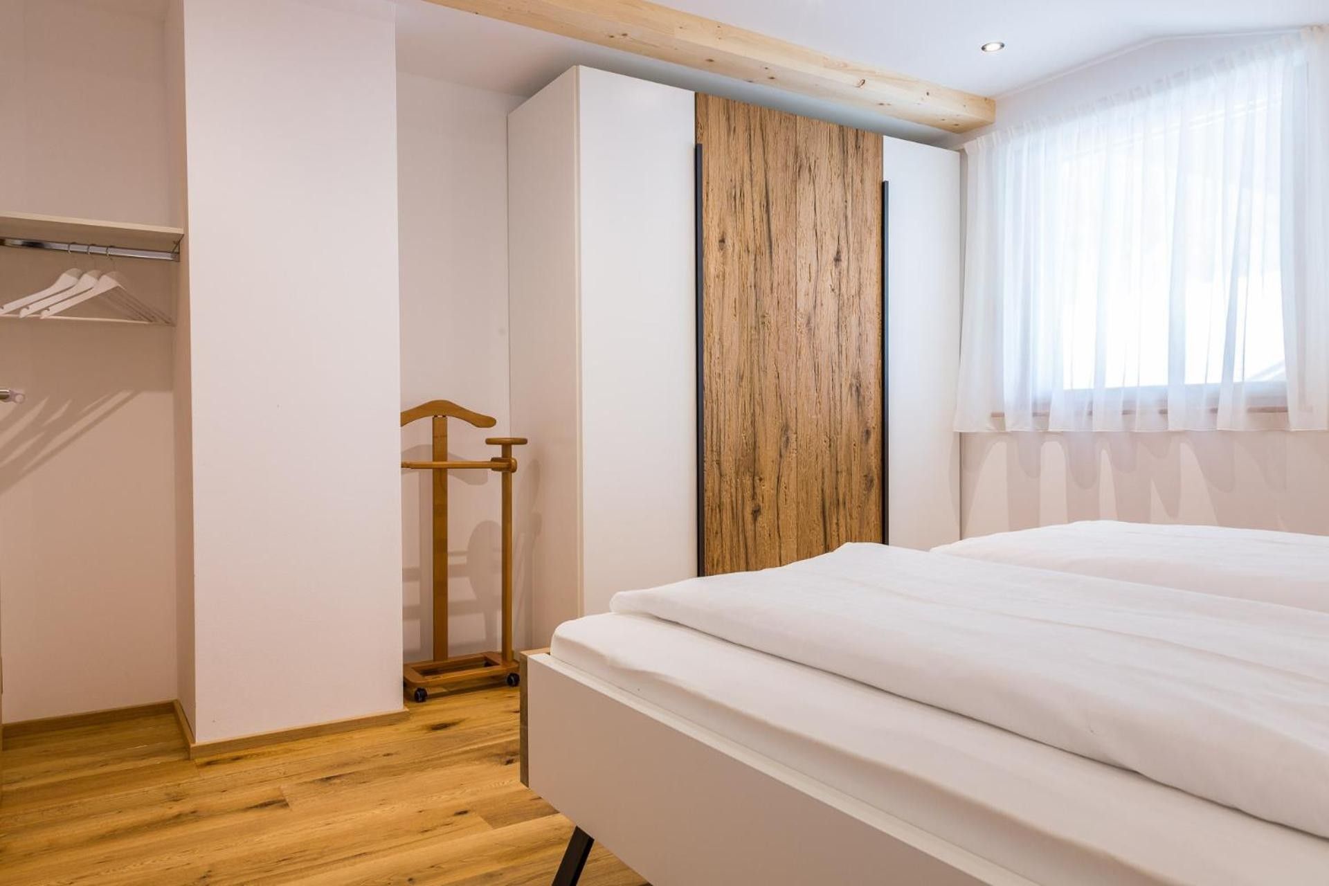 Un dormitorio con una cama, un armario de madera y un ventanal con cortinas.