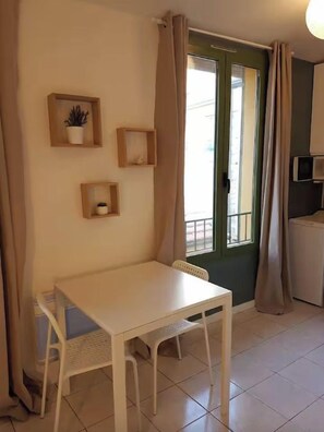 A small room with a white table and chairs, a green door, and a window with curtains.