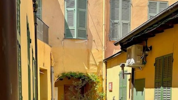Un espace extérieur aménagé avec des tables et des chaises, un petit arbre et un bâtiment aux volets verts.