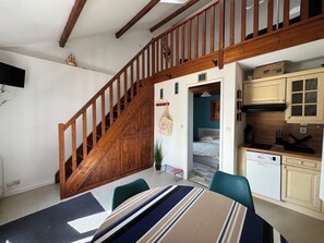 Um quarto com escada de madeira, sala de jantar com toalhas de mesa listradas e cozinha com armários de madeira.