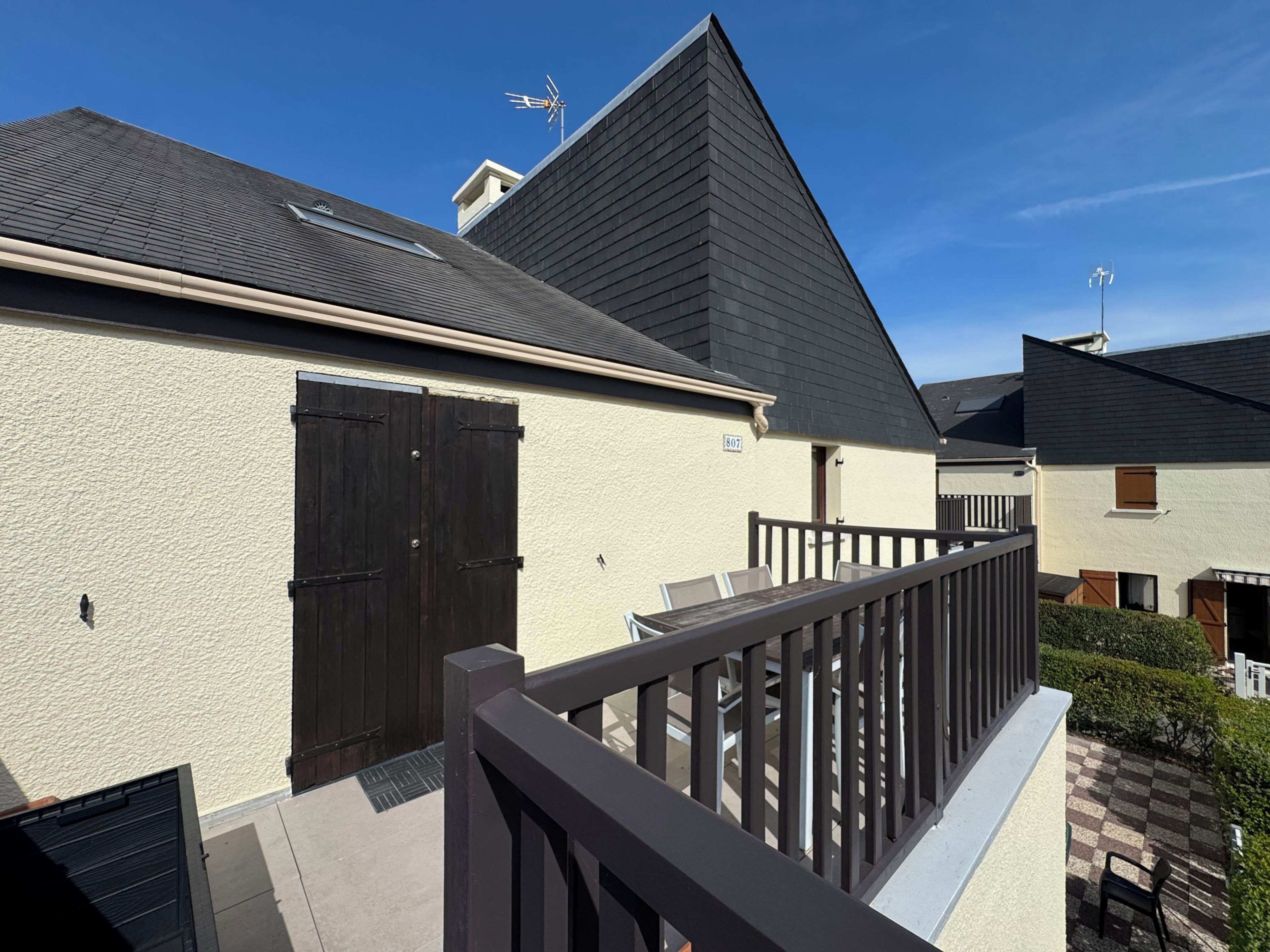 A residential building with a sloped roof, a balcony with a railing, and a small garden area.