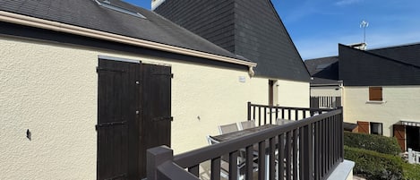 Un immeuble résidentiel doté d’un toit en pente, d’un balcon avec une balustrade et d’un petit jardin.