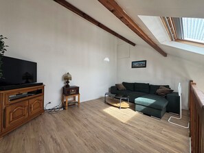 A living room with a television, a small table with a lamp, a sofa, and a wooden cabinet. - Duplex with terrace near beach (Merville-Franceville-Plage)