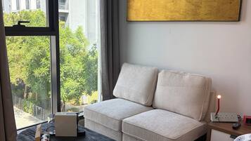 Een moderne hotelkamer met een bank, een bijzettafeltje, een schilderij en uitzicht op een gebouw en bomen.