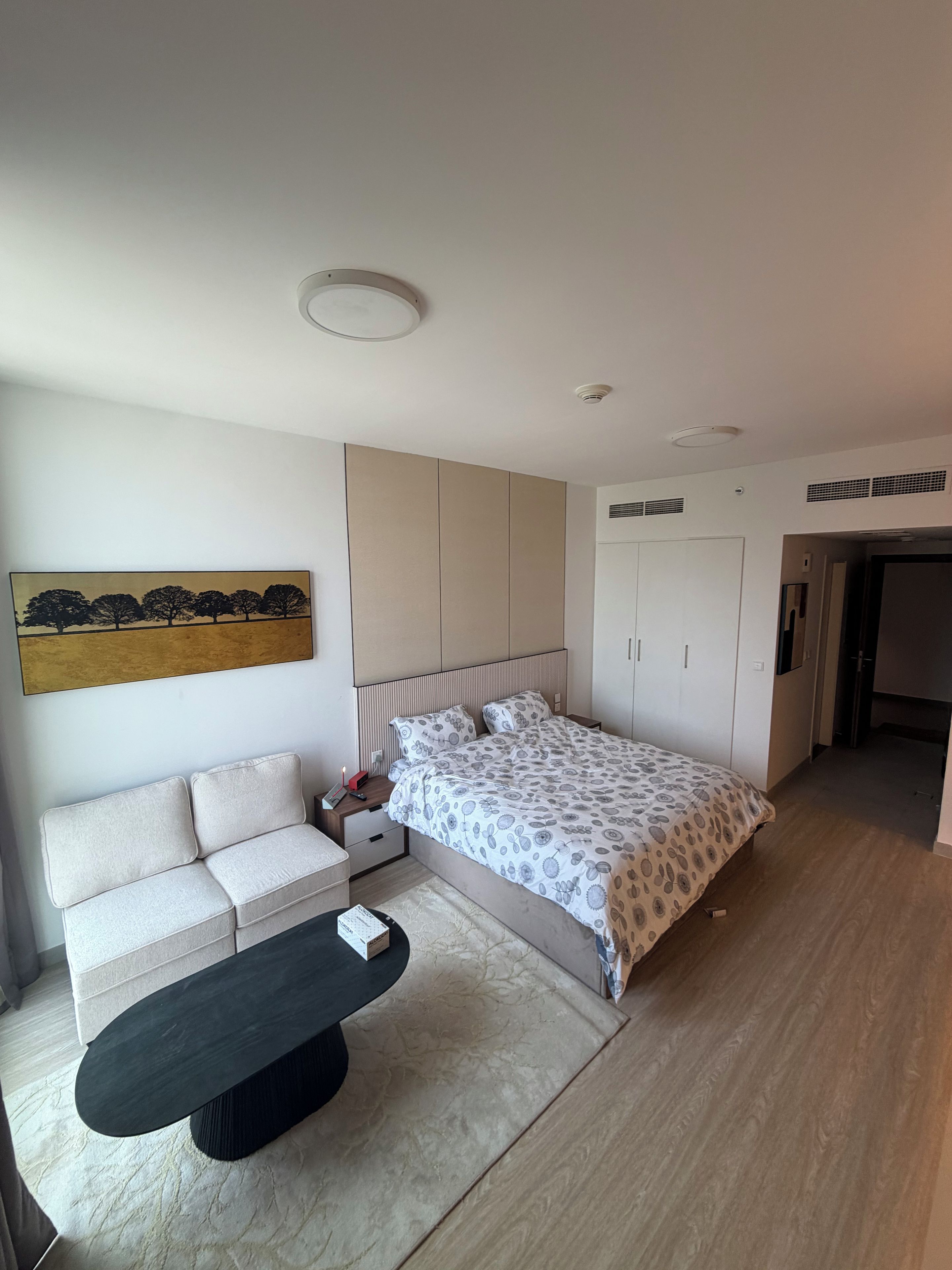 A modern bedroom with a bed, bedside table, nightstand, and a sofa.