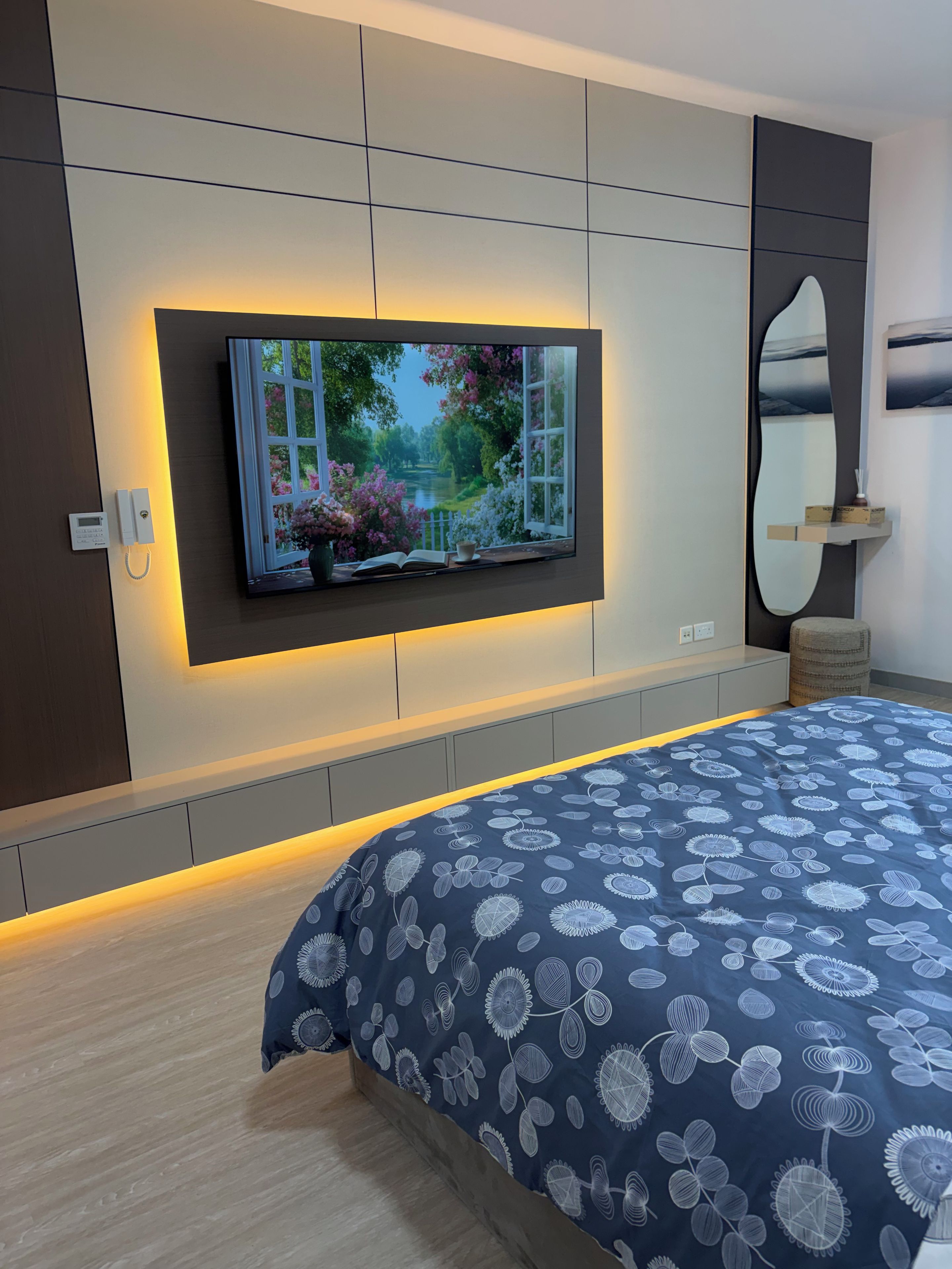 Ein modernes Schlafzimmer mit einem großen Bett, einem an der Wand befestigten Fernseher und einer eingebauten Ablage.