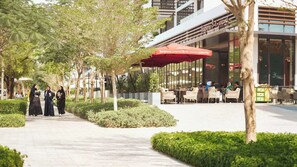 Un café con mesas al aire libre, una sombrilla roja y un edificio moderno al fondo.