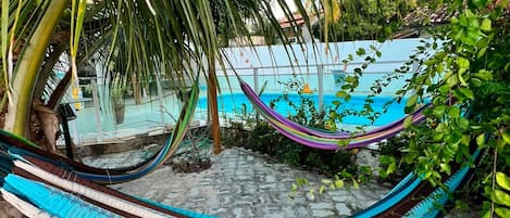 A hammock under a palm tree, a pool, and a stone patio.