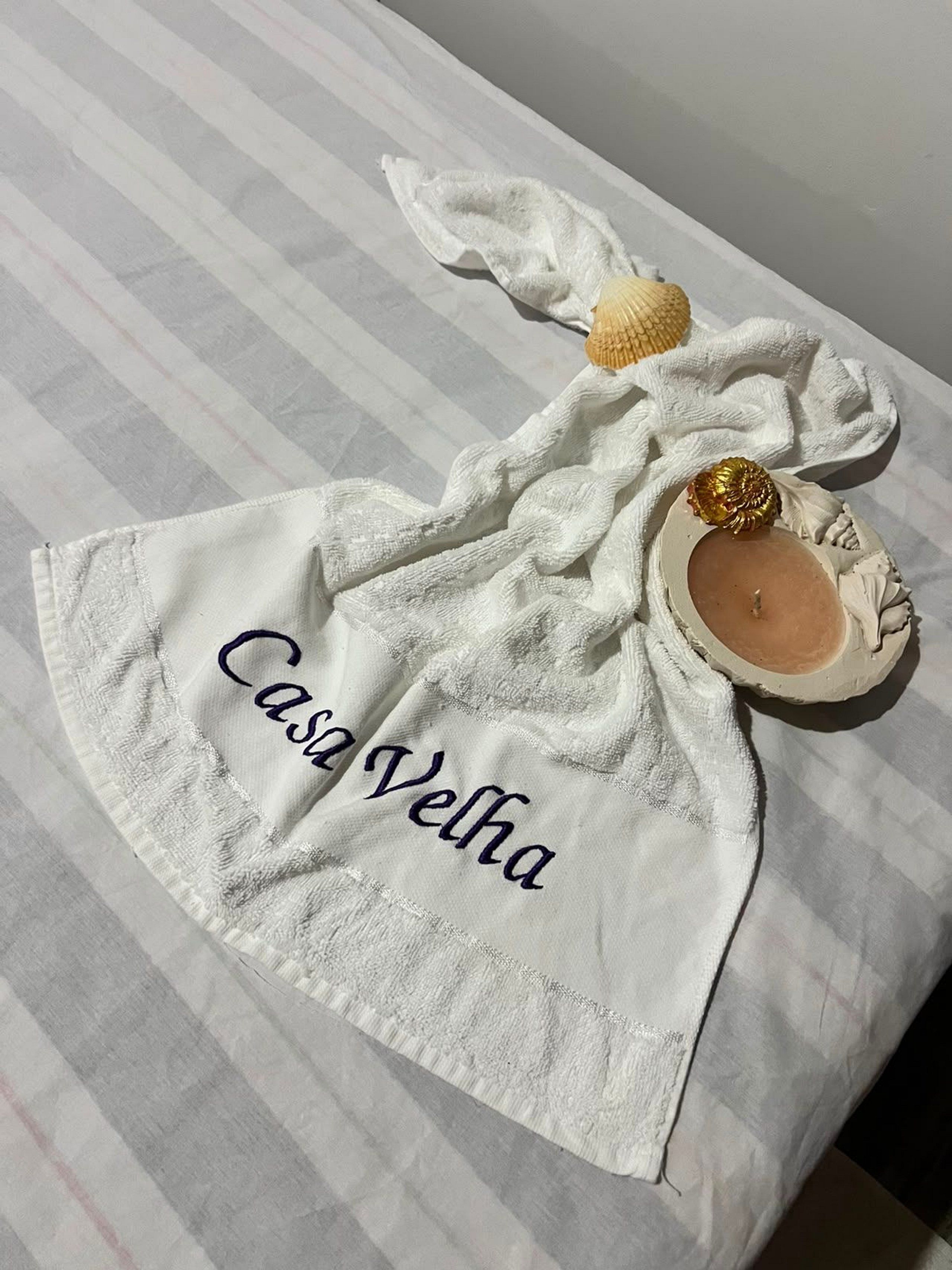 A white towel with 'Casa Velha' embroidered on it, placed on a striped surface.