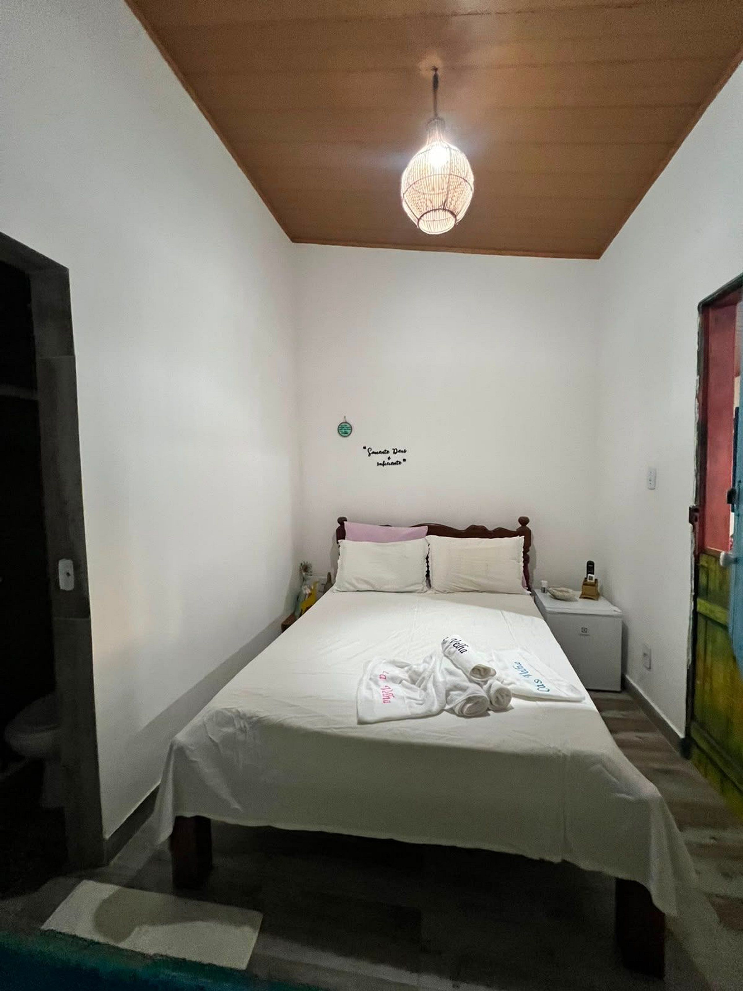 A single-bed room with a wooden ceiling, a bedside table, a nightstand, and a hanging light fixture.