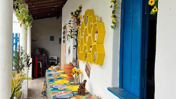 Un'area esterna riparata con un tavolo ricoperto da una tovaglia floreale, una porta blu e uno scaffale esagonale giallo con bottiglie.