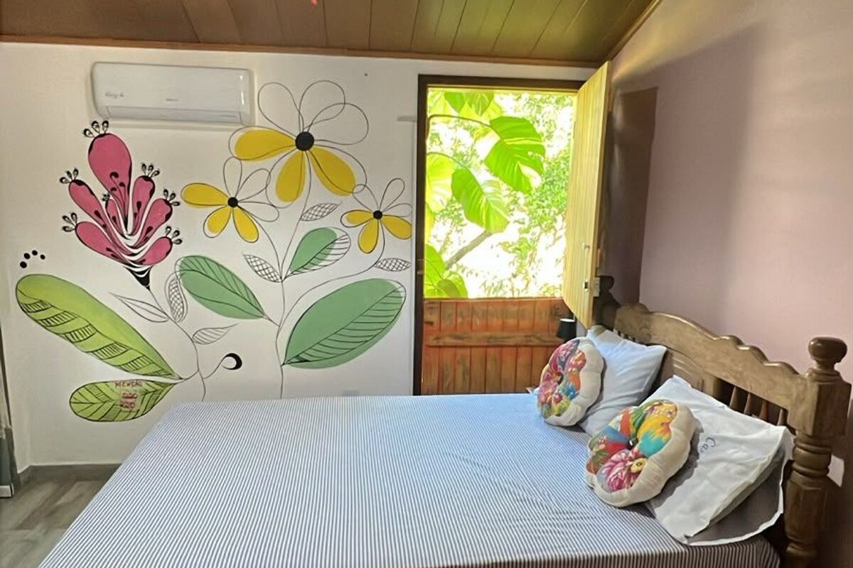 Un dormitorio con una cama, una mesita de noche, una pared con un mural floral y una lámpara de techo.
