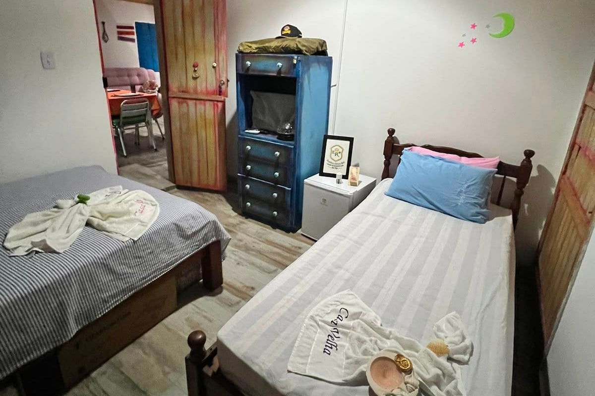 Quarto com duas camas, um guarda-roupa, uma escrivaninha e um candeeiro suspenso.