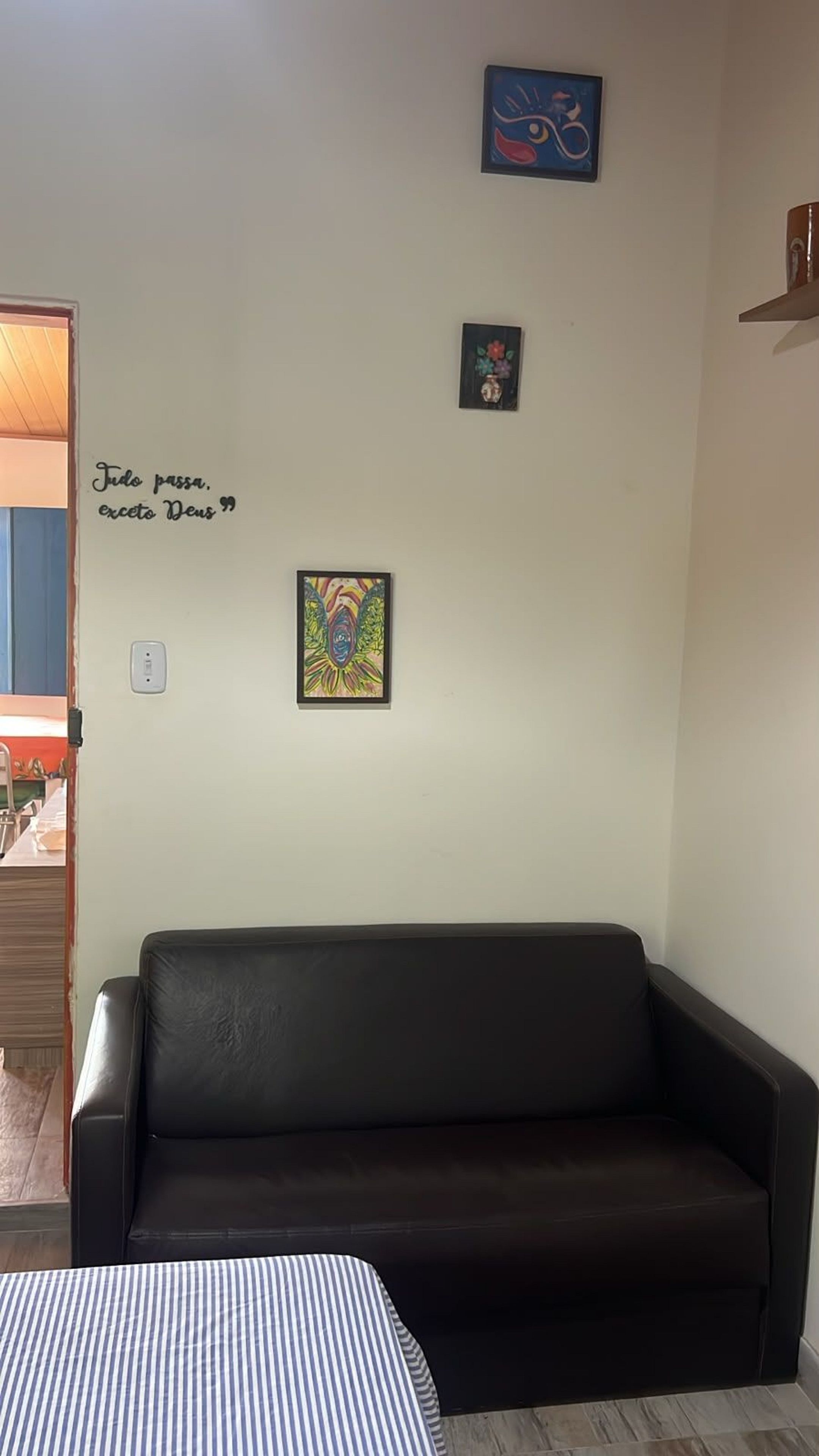 A room with a black leather sofa, a bed with a striped bedspread, and three wall-mounted artworks.