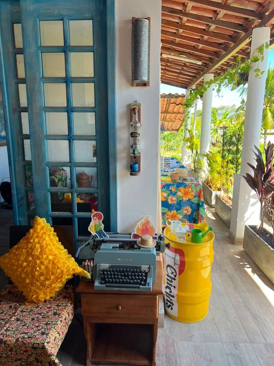 A room with a blue door, a typewriter, a yellow barrel, and a table with a floral tablecloth.
