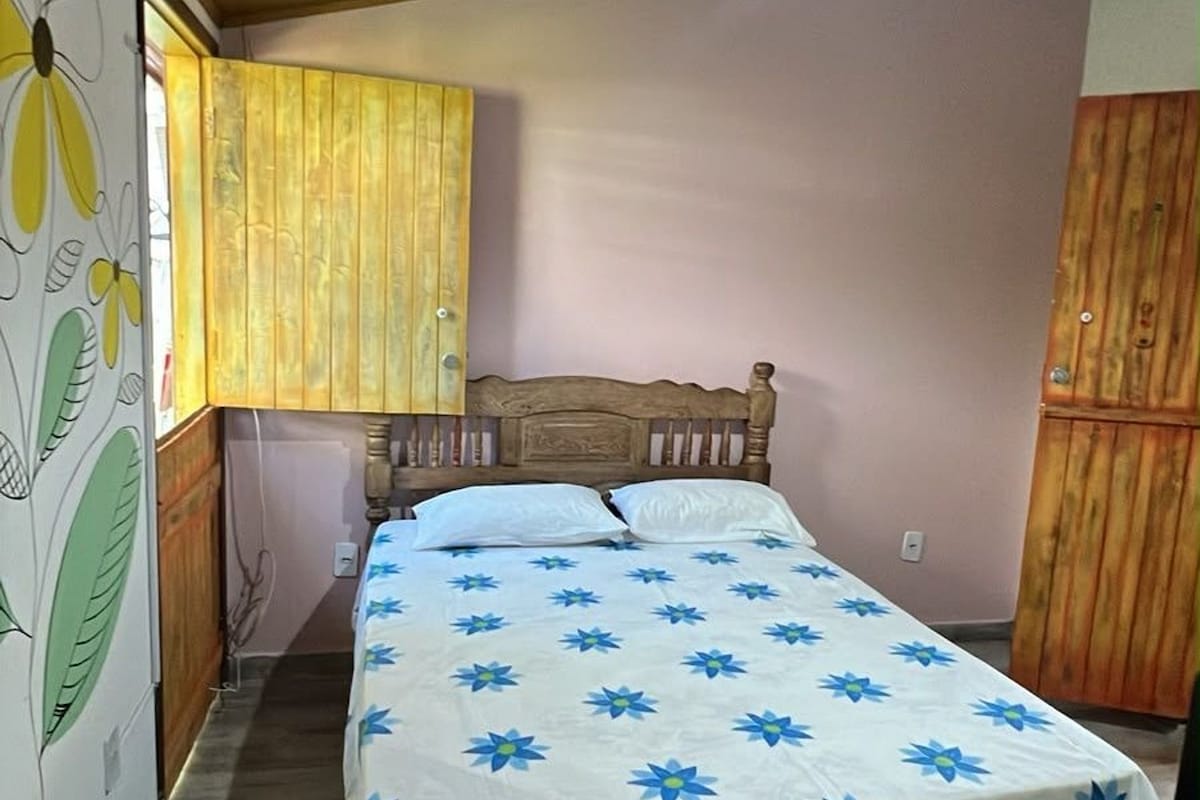 Un dormitorio con una cama de madera, una ventana con cortinas amarillas y una pared con un mural floral.