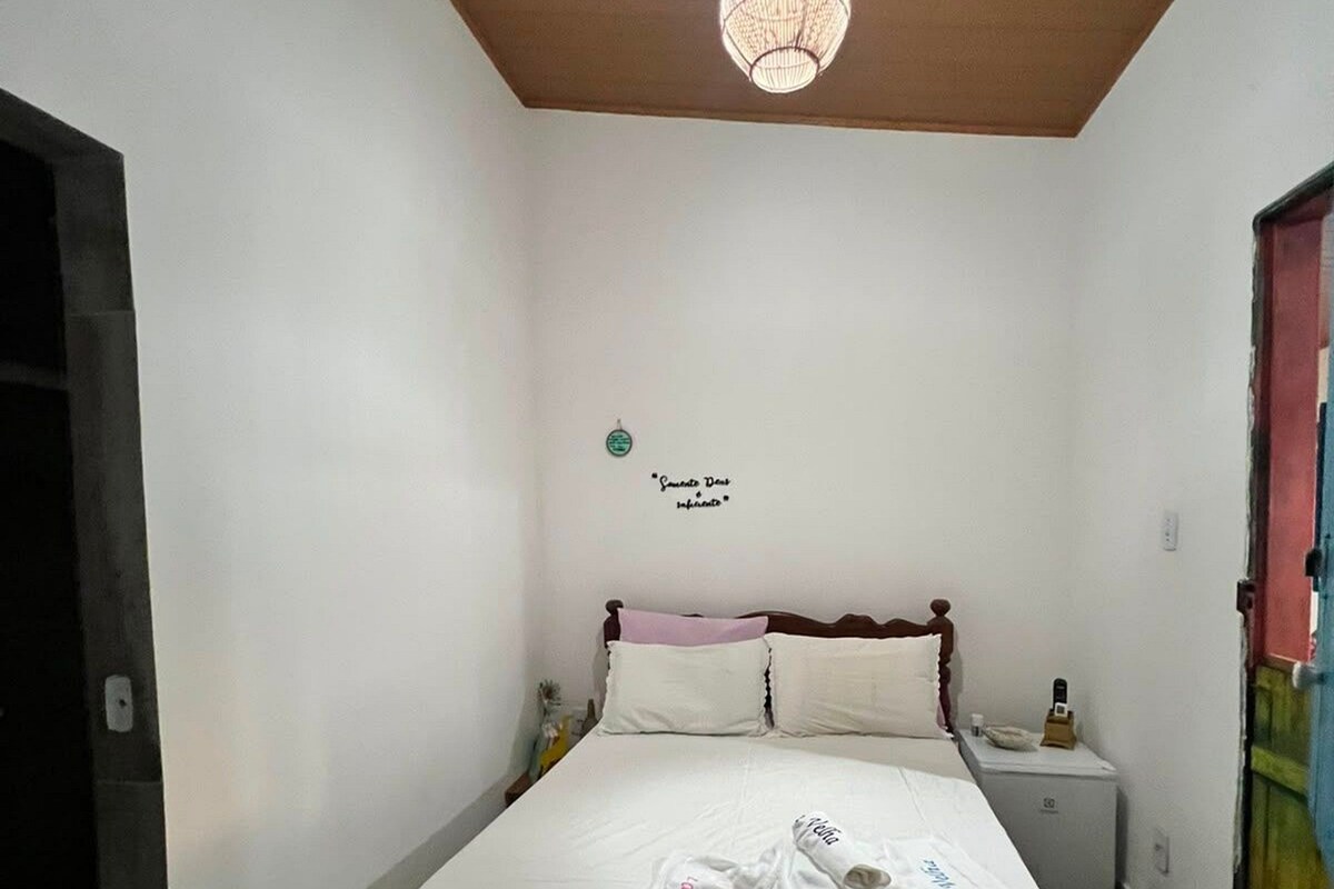 Quarto individual com uma cama, teto de madeira, mesa de cabeceira e luminária pendente.
