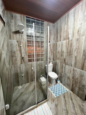 Casa de banho com cabine de duche de vidro, sanita e um tapete xadrez.