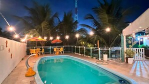 A swimming pool with a curved edge, surrounded by palm trees and outdoor seating. - Casa Velha Hospedagem Jacuípe (Camaçari)