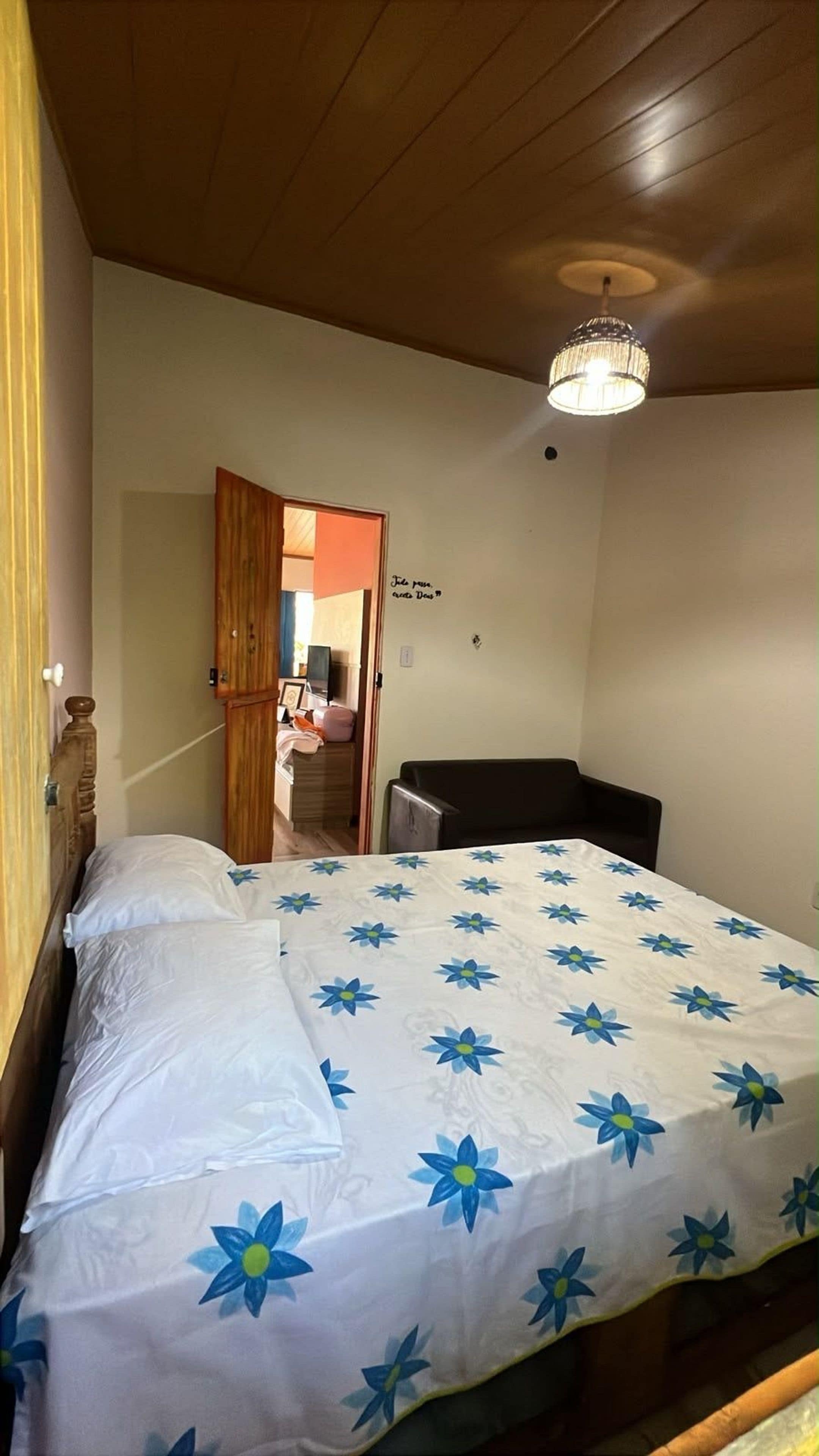 Una habitación con una cama, techo de madera, candelabro y una puerta que da a otra estancia.
