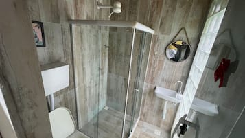 Chuveiro com porta de vidro, pia branca e espelho na parede.