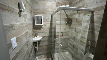 Un baño con ducha separada por vidrio, un lavamanos blanco y un inodoro.